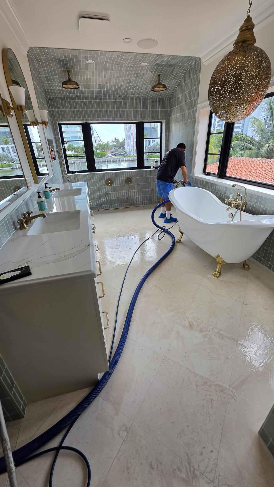 Owner of Keep It Clean Tile and Grout running a low moisture extraction wand across a shellstone floor in a Miami Beach master bathroom, hose routed over the stone and the surface damp from the pass rather than flooded