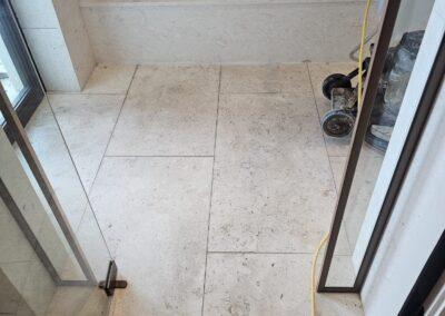 Shellstone limestone shower floor and built-in bench in Miami Beach before the old sealer was stripped, with a rotary floor machine in the shower