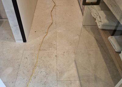 Shellstone limestone bathroom floor in Miami Beach before cleaning, with the cabinetry covered in plastic and the base taped off