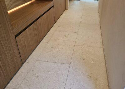 Shellstone bathroom floor in Miami Beach after deep cleaning and sealing, running past wood cabinetry to the glass shower